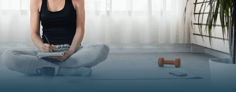woman takes a break from yoga to write in a journal about national wellness month.